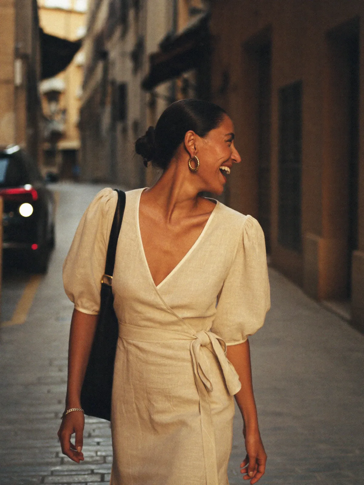 An elegant woman laughing on a sunlit Mediterranean street at golden hour