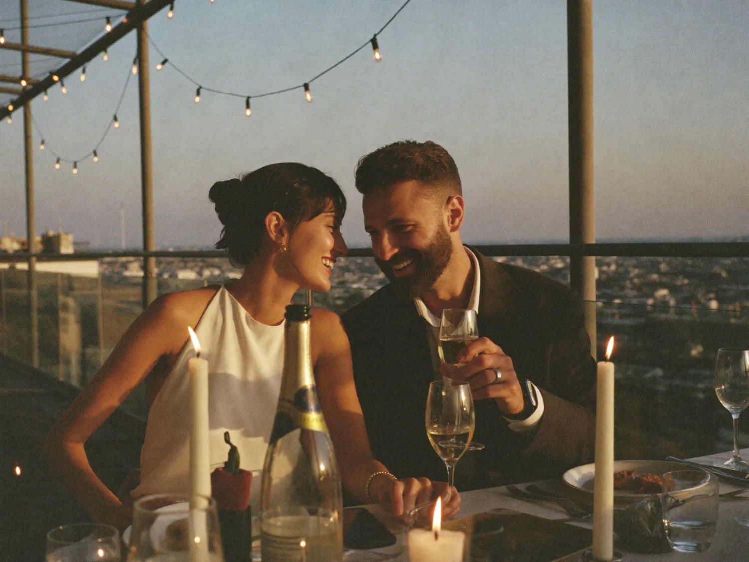 A couple sharing a candid, joyful moment over champagne at a rooftop dinner